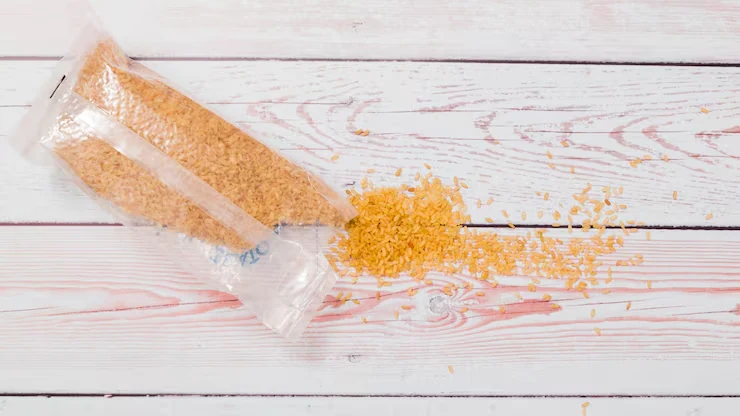 Yellow grains spilling from a clear bag onto a pale wooden surface