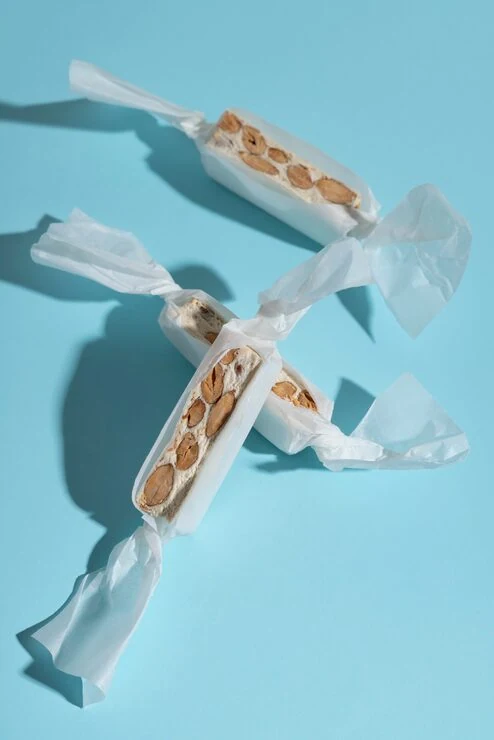 Two nougat bars in opened white wrappers on a blue surface
