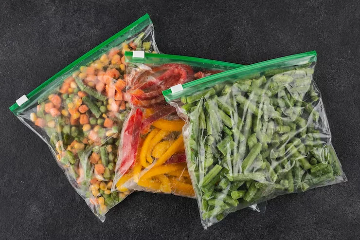 Three clear slider-closure bags filled with vegetables on a dark surface