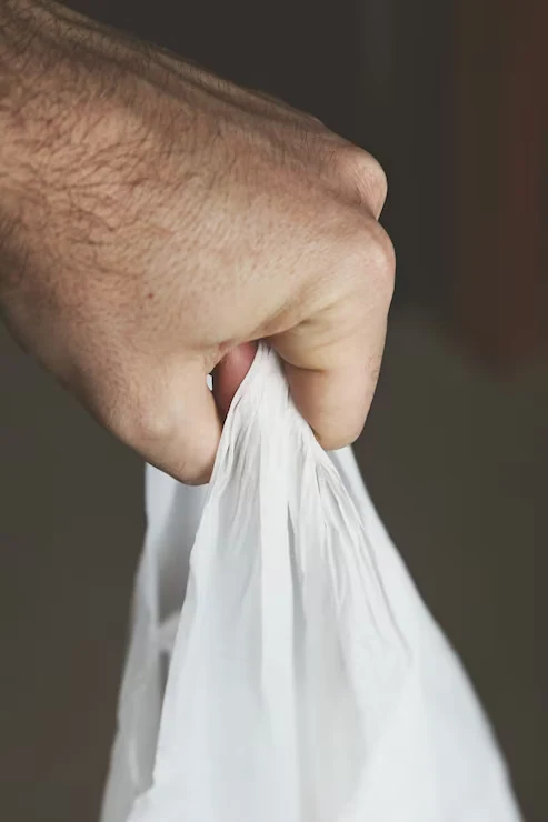 A hand holding the handle of an unprinted white plastic carry bag