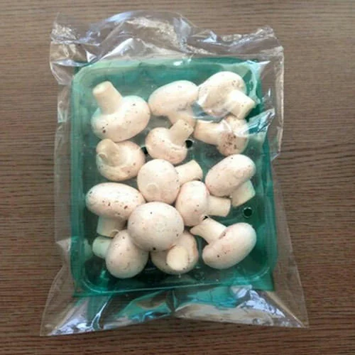 Button mushrooms in a green tray with a clear film overwrap